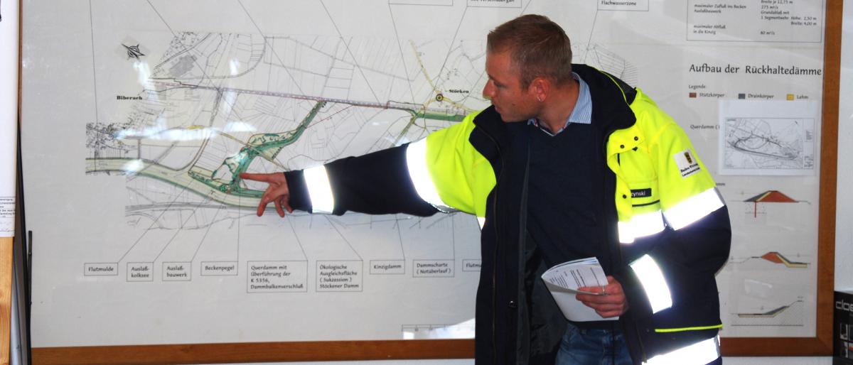 Ein Stauwärter erklärt an einer Karte Deteils von Hochwasserrückhaltebecken.